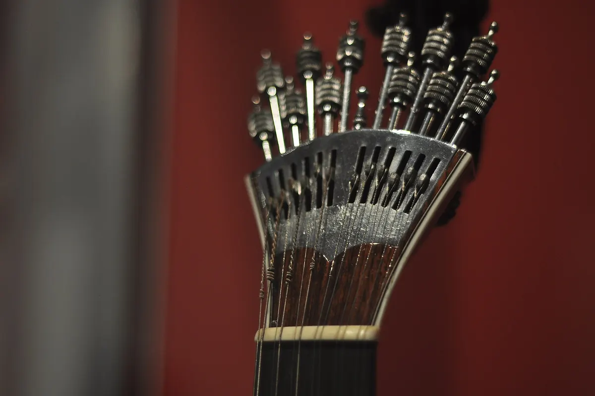 The fan-shaped metal tuning mechanism of a Portuguese guitar with its row of tuning keys, against a red background.